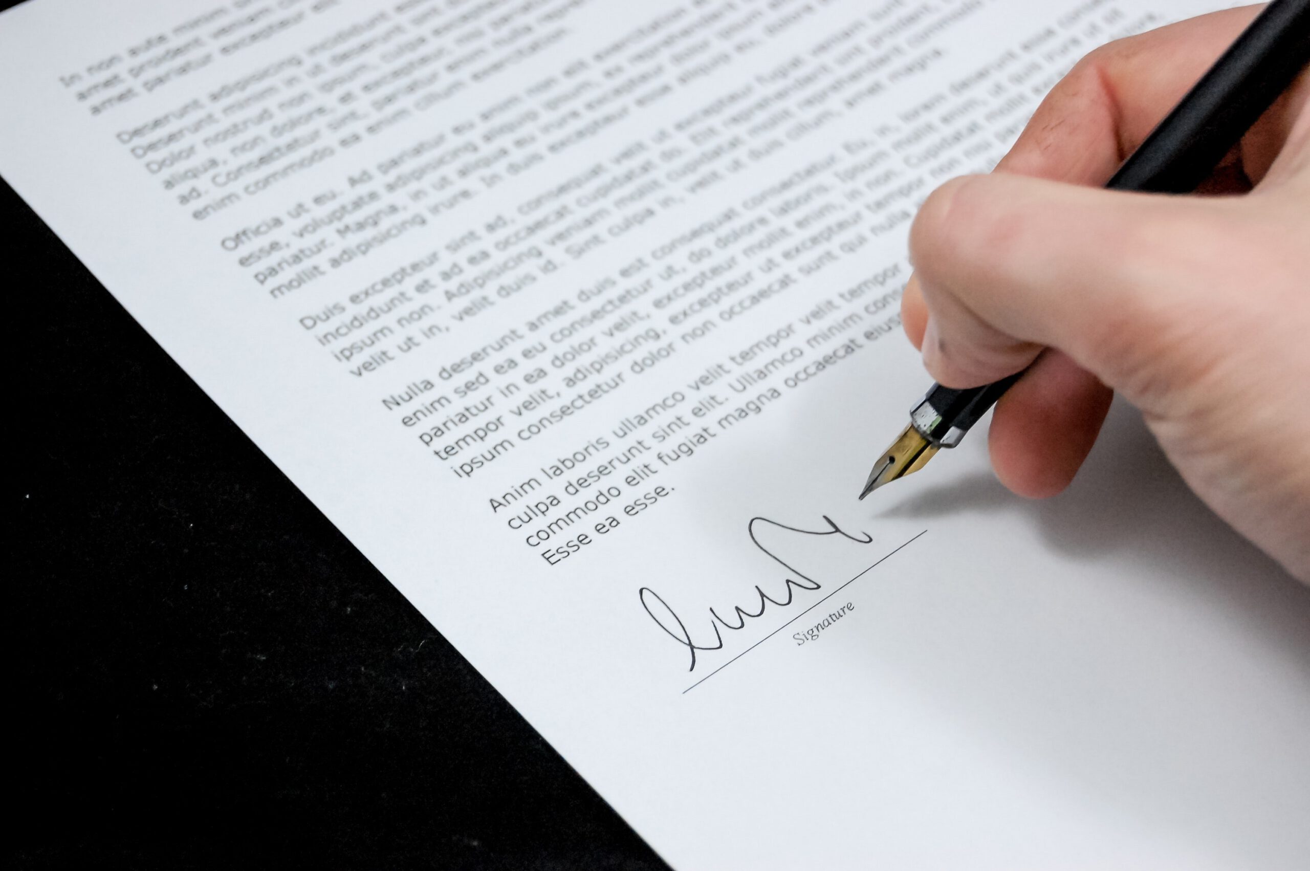 Dłoń mężczyzny podpisująca piórem dokument