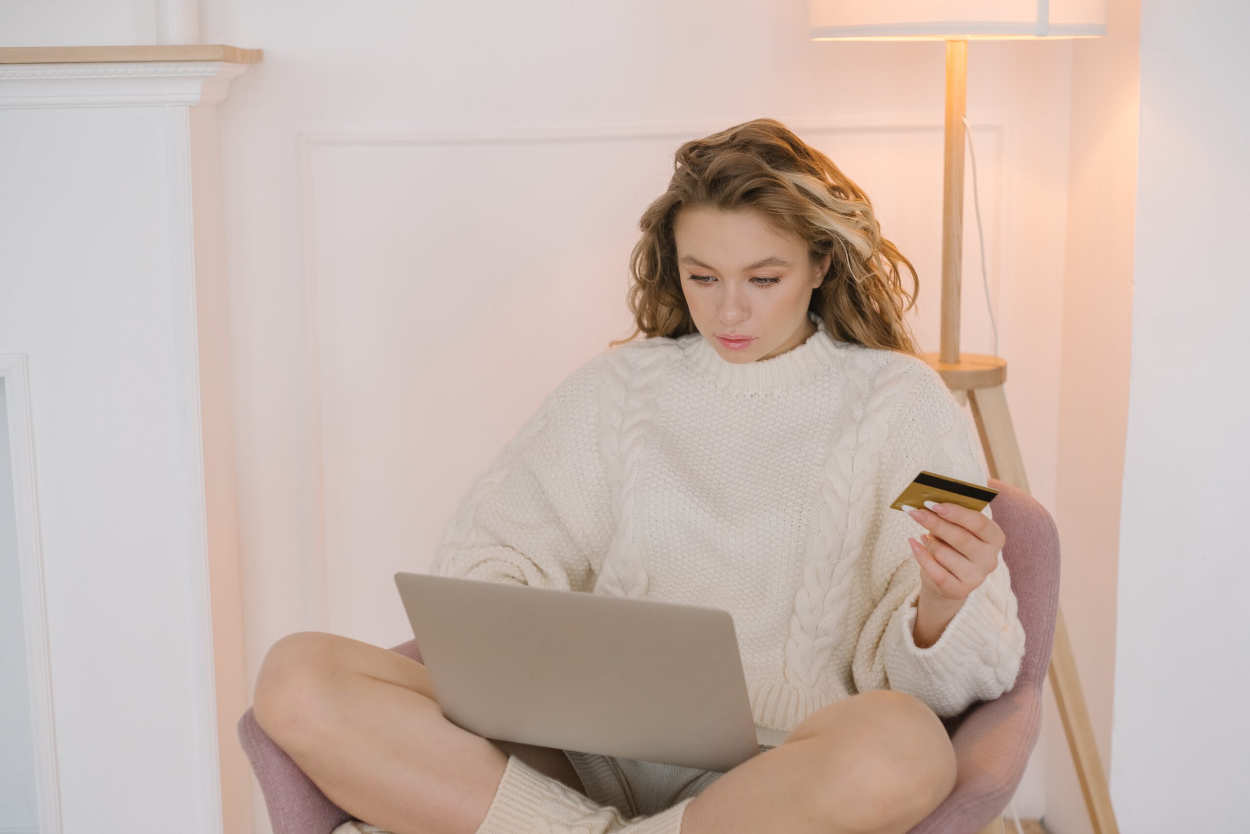 Kobieta siedząca na fotelu z laptopem na kolanach i kartą kredytową w dłoni