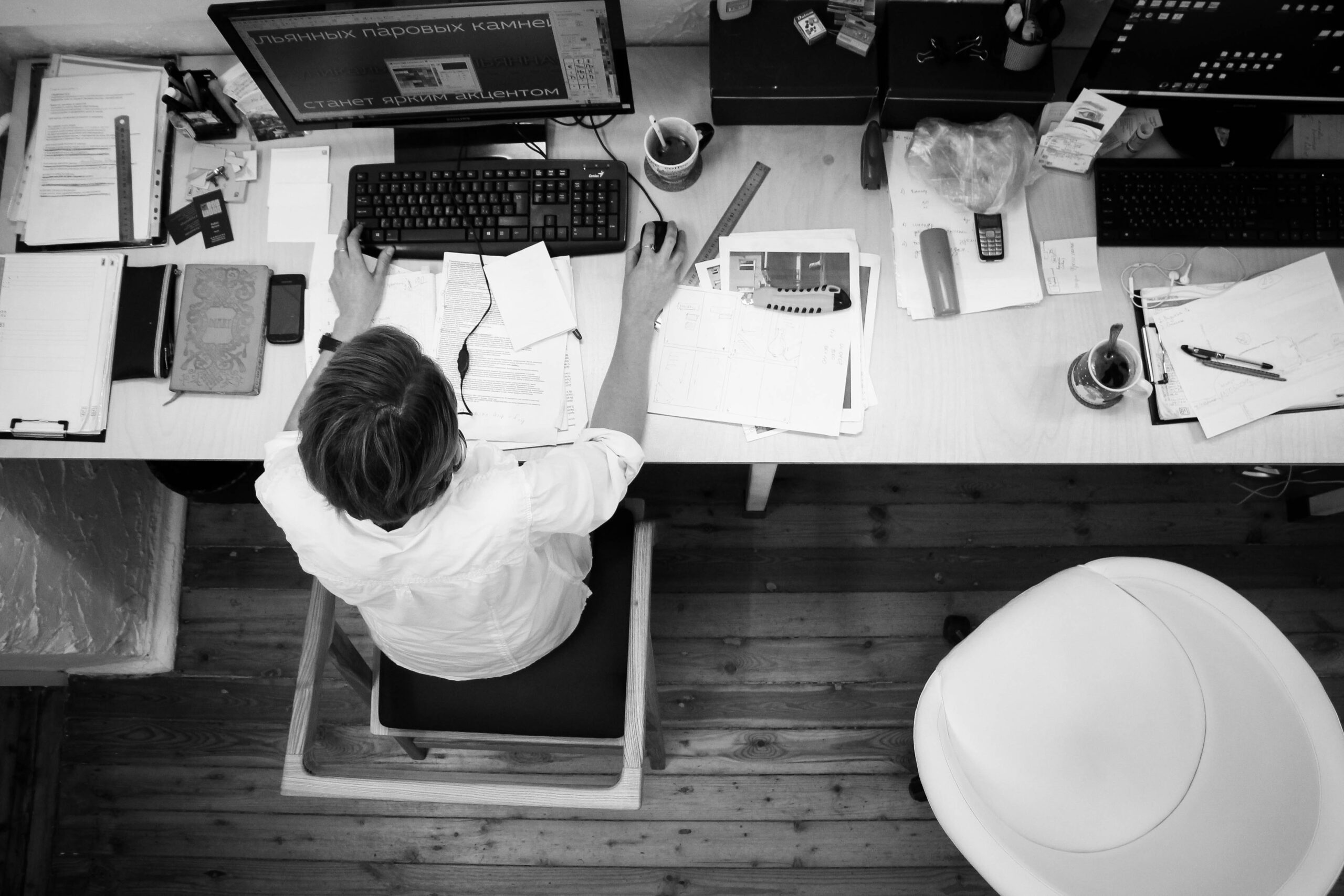 Widok z góry na kobietę siedzącą w biurze i pracującą na komputerze przy biurku zawalonym różnymi przedmiotami